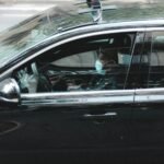 Side view of African American male driver in mask driving black taxi on road in downtown of big city at  daytime